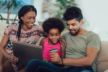 Cute little Afro-American girl and her beautiful young parents using a laptop and doing shopping...