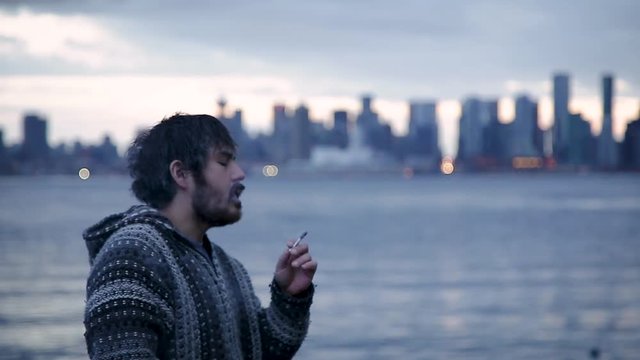 A young man smoking a joint with downtown Vancouver, BC, in the background.