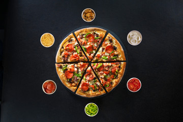 Flat lay of italian pizza and fresh ingredients around on dark surface top view