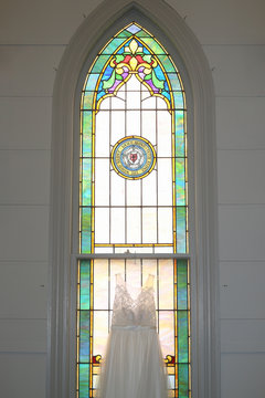 Wedding Dress Hanging In Stained Glass Church Window