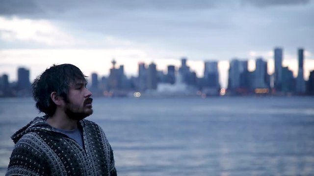 A young man smoking a joint with downtown Vancouver, BC, in the background.