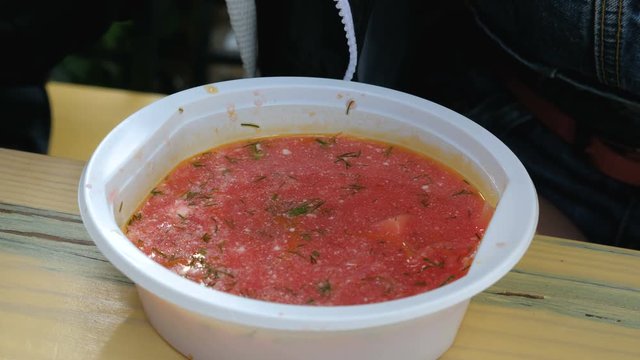 Tourist eats borscht from plastic dishes in an outdoor cafe. Close up.