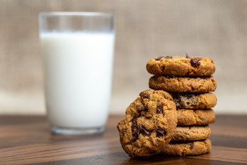 Tasty cookie with creamy chocolate drops, with a glass of milk defocused in the background.