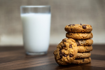 Tasty cookie with creamy chocolate drops, with a glass of milk defocused in the background.