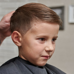 Cheerful Caucasian boy  getting hairstyle in barbershop.