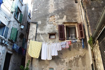 Croatia, Rovinj, August 2018: Adriatic, streets of a small seaside town, sunny hot summer day, old weathered houses, windows with multi-colored shutters, drying clothes on ropes, yachts, blue sea.