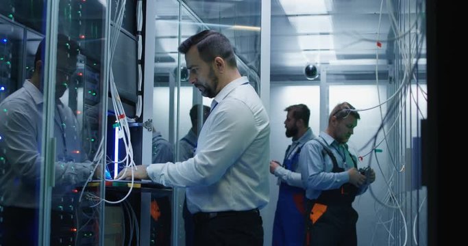 Medium shot of three people working in a data center with cable to repair rows of server racks