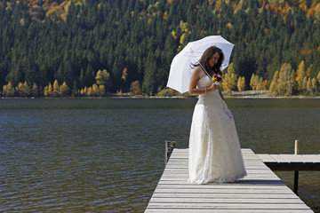 Obraz premium Single bride in wedding dress and holding a white umbrella walking on a ponto