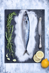 flatlay of fresh fish on a slate stone plate decorated with rosemary, garlic, lemon slices and knife. food background