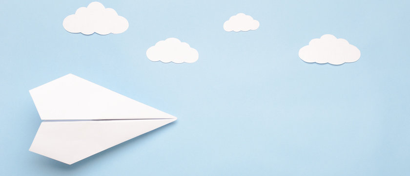 Fototapeta Flying paper plane in the clouds on a blue background. Concept of flight, travel, transfer. Top view, copy space, flat lay, banner