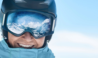 Close up of the ski goggles of a man with the reflection of snowed mountains.  A mountain range...