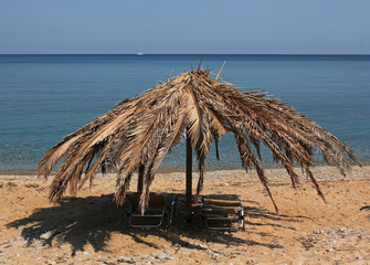 Fototapeta na wymiar Palm leaves umbrella on the sandy beach, sailboat on blue sea in background
