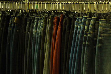 Obraz premium Jeans of different colors on hangers in a clothing store. Tinted in a yellow dark key. Background for design on the theme of fashion or second hand. The concept of shopping and sales.