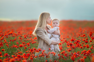 Happy motherhood. Mom and son daughter are playing in the field of flowering red poppies