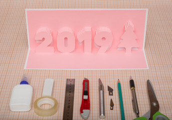Making  pop-card  in the form of 2019 year. Handmade card and tools  used for its construction on milliliter paper.