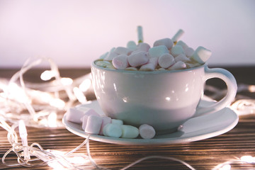 hot chocolate with marshmallow candy and Christmas decorations garland on a wooden background