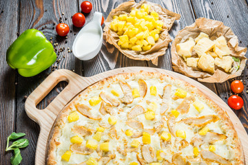 Macro. Big pizza with chicken and pineapples on a round cutting board on a dark wooden background. Ingredients.