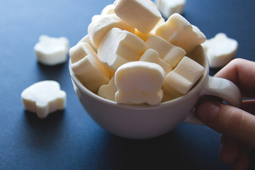 marshmallow in the form of bears in a white cup holds a hand on a dark background. clouse up