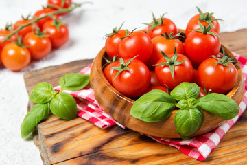 Wooden bowl with fresh ripe cherry tomatoes and basil leaves on a table with red checkered towel, healthy food, top view