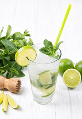 Mojito cocktail with fresh limes and mint leaves in a glass on a light grey stone background