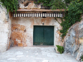 A stone shelter carved out of a cliff with green vegetation wooden doors and a striped awning