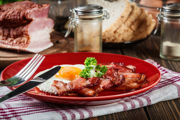 Slices of smoked bacon and fried egg on a red plate