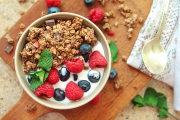 Healthy breakfast. Granola, muesli with yogurt and fresh berries in a bowl on wooden background, top view, flat lay.