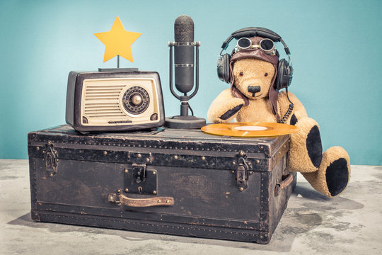 Retro radio, studio microphone, vinyl disc and golden star on old aged classic travel trunk and DJ Teddy Bear toy with leather aviator's hat, headphones and goggles. Vintage style filtered photo