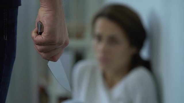 Aggressive man with knife abusing scared wife, scared woman sitting on floor