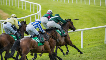 Group of jockeys and race horses galloping down the track