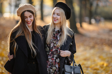 Two pretty girls walk on the city street, talk and smile to each other