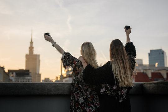 Two gitls stand on the rooftop and have a drink