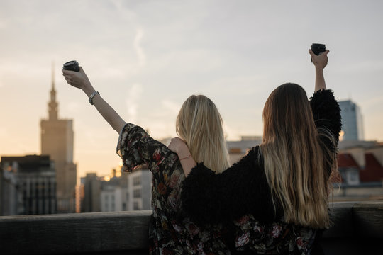 Two gitls stand on the rooftop and have a drink