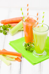 Carrot and celery juice with fresh vegetables on bark plates on wooden background.