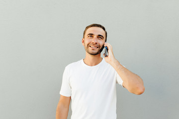Smiling man talking by smartphone while holding his head and looking at the camera over grey background