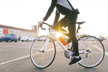 Fototapeta premium Portrait of an attractive cyclist in motion. Young rider in dark bike wears a bike on a street background and sunshine in the sunset. Transport and people.Cycling as a hobby