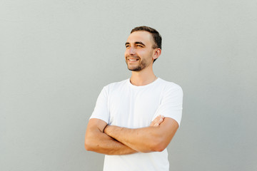 Confident young handsome man keeping arms crossed and smiling while standing against gray background