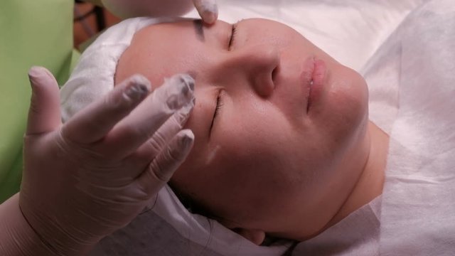 Facial massage of a Asian girl in a beauty salon. Close-up of hands of the beautician in white gloves during the procedure in the cosmetology center.