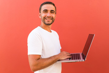Handsome programmer man with laptop on red background