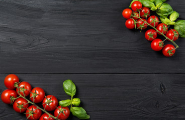Ripe red cherry tomatoes with fresh basil leaves on black wooden table, top view with copy space