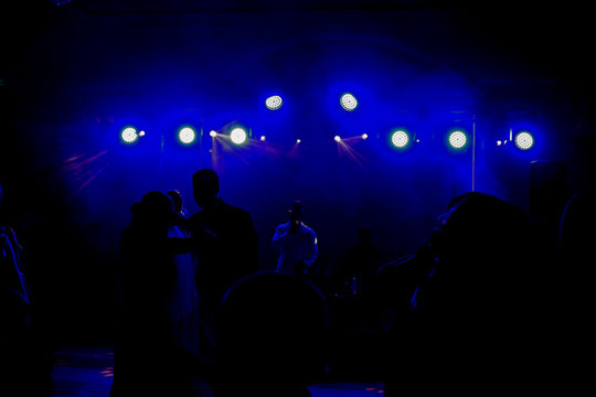 Blue light shine over dancing people in the darkness in front of a stage with a band and a singer on it