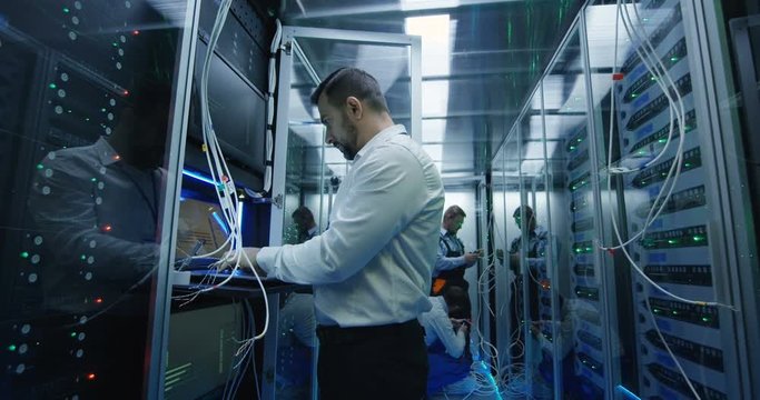 Medium shot of a manager performing an inspection while working in a data center inbetween rows of server racks