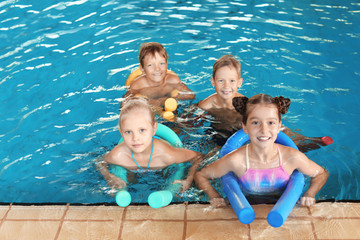 Little kids with swimming noodles in indoor pool