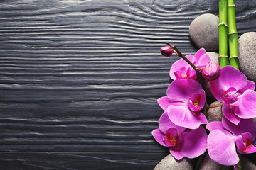 Spa stones with orchid flowers and bamboo on dark wooden background, top view. Space for text