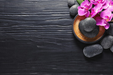 Composition with orchid flowers and spa stones on dark wooden background, top view. Space for text