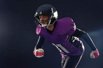 American football player in uniform running on dark background