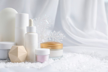 Fototapeta na wymiar Set of cosmetic products and decorative snow on white fabric, space for text. Winter care
