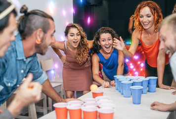 Group of happy friends playing beer pong in pub cocktail bar - Young millennials people having fun...