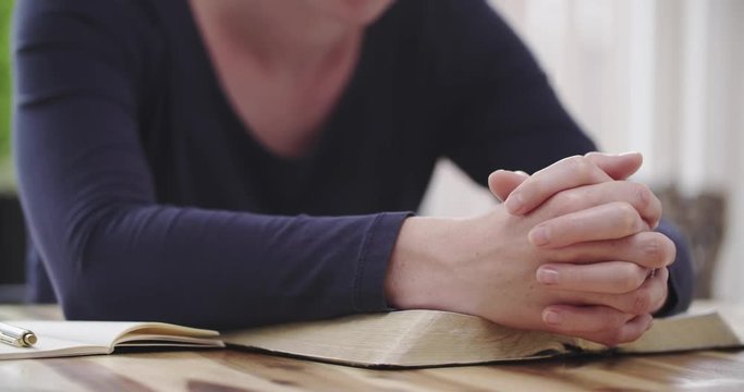 Christianity and faith concept - a handheld closeup shot of a woman praying over an open Bible at home.