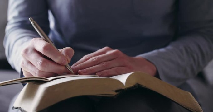 Handheld closeup shot of a woman studying the Bible at home and taking notes.